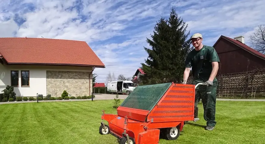Mężczyzna z wertykulatorem na trawniku. Wertykulacja latem to klucz do zdrowej, zielonej murawy.