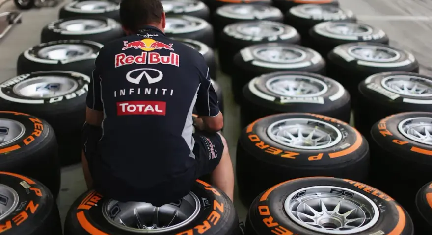 Mechanik w stroju Red Bulla siedzi wśród rzędów opon F1.