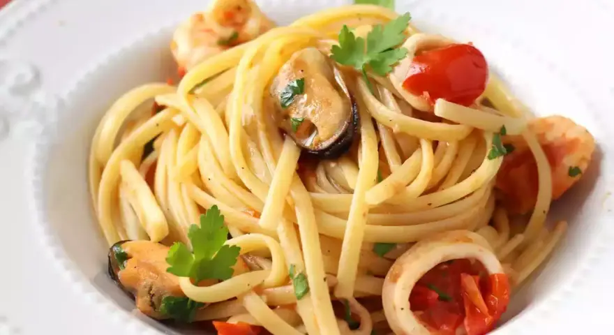 Tallarines con gambas al ajillo, mejillones y calamares, salpicados con perejil fresco y trocitos de tomate.