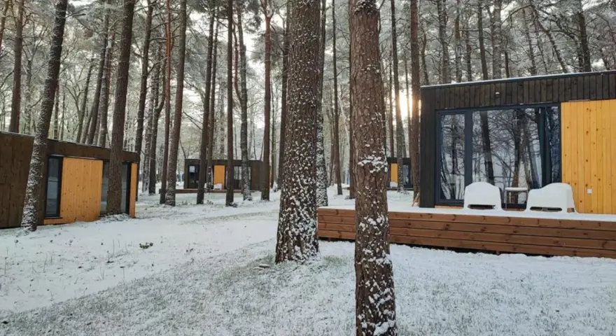 Nowoczesne domki nad morzem całoroczne w zimowej scenerii. Śnieg pokrywa trawę i drzewa, tworząc bajkowy krajobraz.