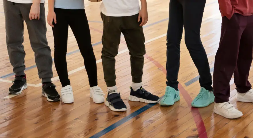 Dzieci na sali gimnastycznej, zastanawiające się, jakie buty na WF do szkoły wybrać. Różne modele sportowego obuwia na drewnianej podłodze.