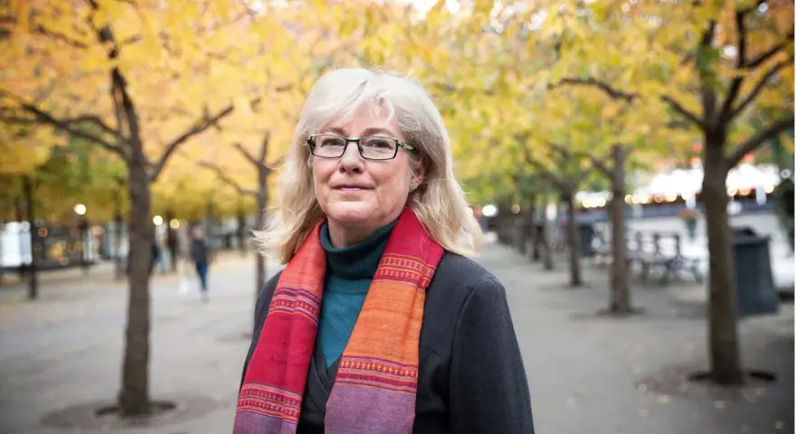 Kvinna med glasögon och färgglad scarf i höstpark. Hon verkar inte ha ont i leder brist på energi, utan njuter av den vackra naturen.