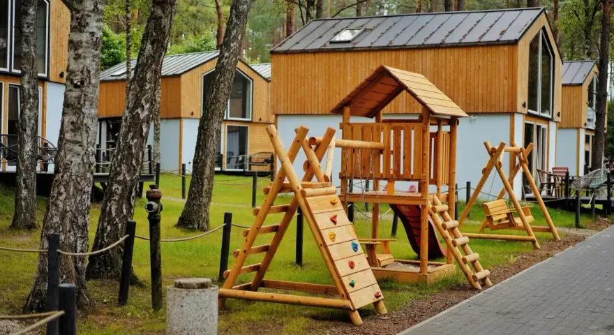 Drewniany plac zabaw z domkami w tle. Idealne bory tucholskie atrakcje dla dzieci, gdzie można odpocząć i pobawić się na huśtawkach i zjeżdżalni.