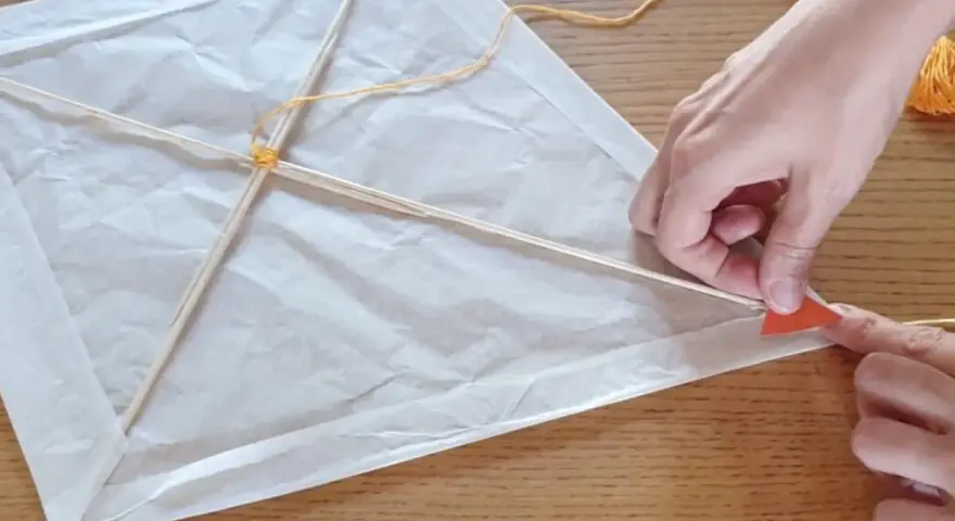 Mains fabriquant un cerf-volant en papier blanc avec des bâtons de bois et de la ficelle.