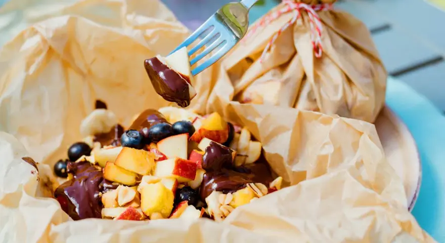 Fruchtiger Nachtisch vom Grill: Apfelstücke, Blaubeeren und Bananen mit Schokoladensauce, serviert in Papier.