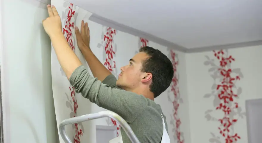 Mann tapeziert mit roter Blumenmuster-Tapete die Decke.