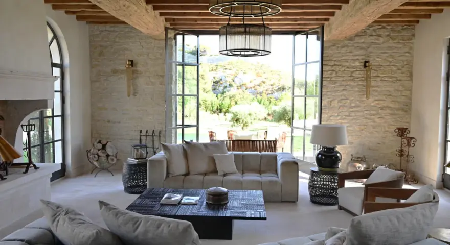 L'intérieur d'un mas provençal baigné de lumière, avec des poutres apparentes, des murs en pierre et une vue imprenable sur la campagne.