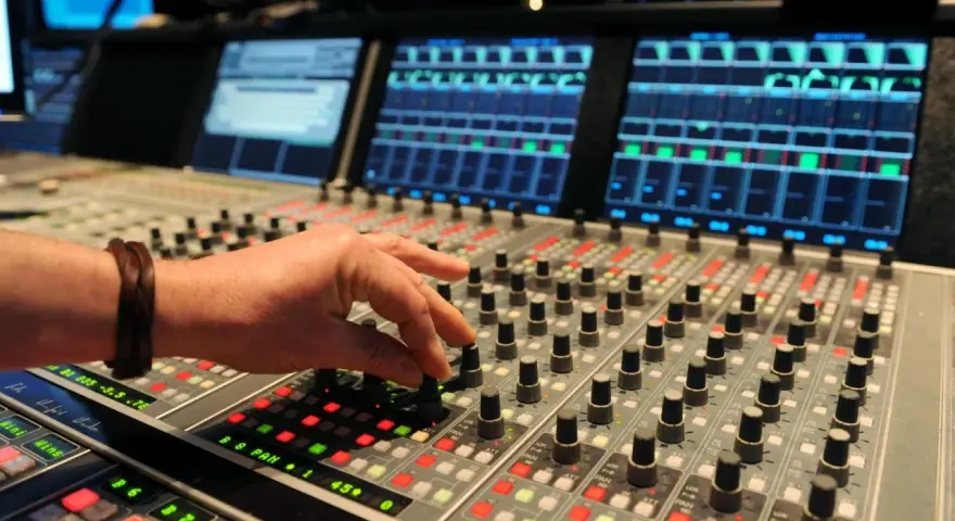 Hand am Mischpult, das an die Erfindung von Autotune erinnert. Tontechniker regelt Regler.