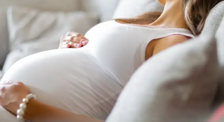 Kobieta w ciąży odpoczywa na kanapie, delikatnie głaszcząc brzuch. Szuka odpowiedzi na pytanie: co na mdłości w ciąży, by poczuć się lepiej.
