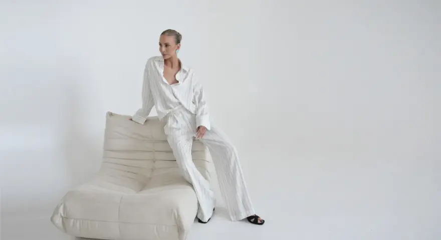 Elegancka kobieta w pasiastym komplecie, uosobienie quiet luxury, siedzi na kremowej sofie.