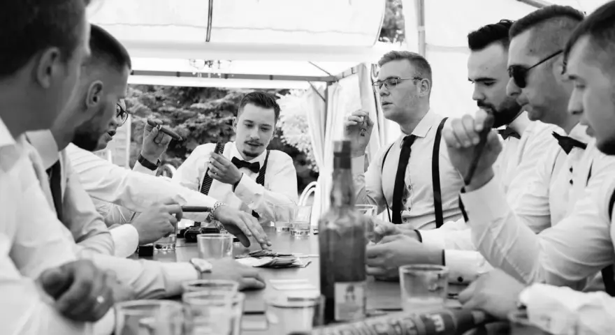 Panowie w eleganckich koszulach i szelkach świętują, paląc cygara i pijąc. Świetne kawalerski pomysły na wspólne chwile.