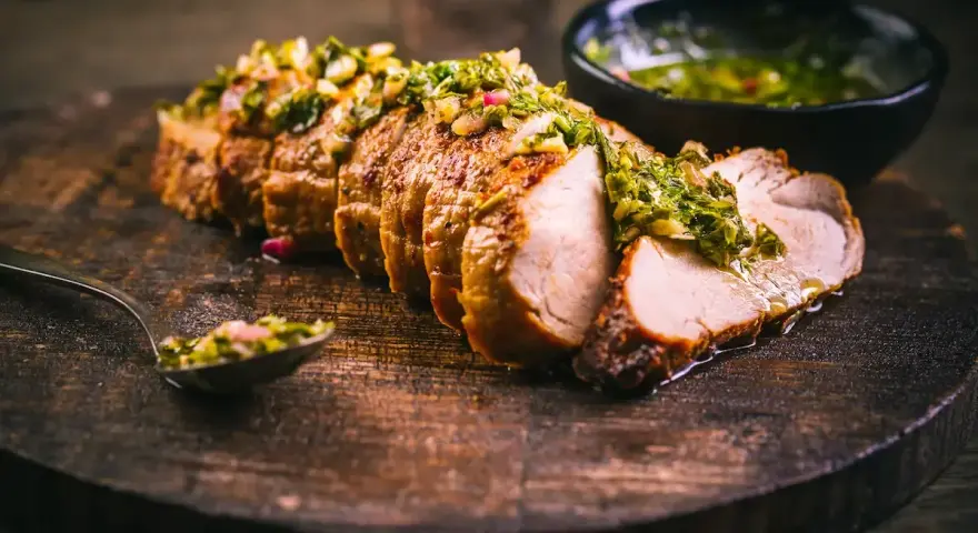 Jugoso solomillo de cerdo, cortado en rodajas y cubierto con una sabrosa salsa verde, servido en tabla de madera.