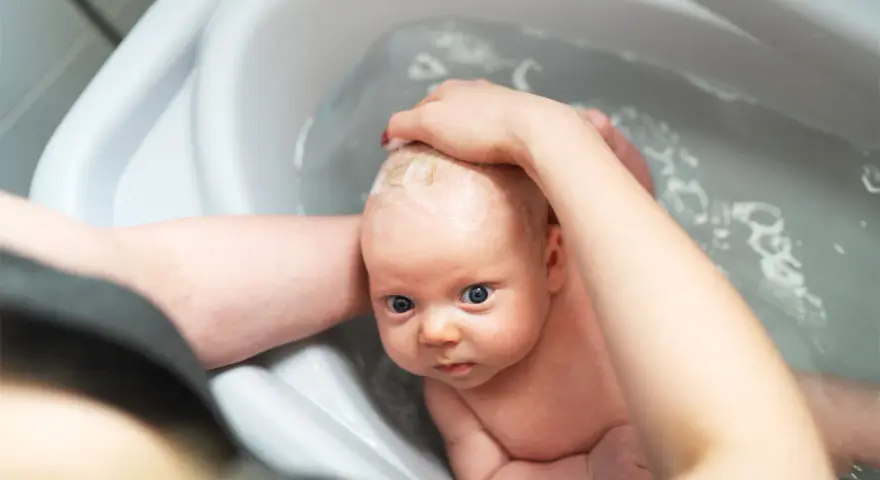 Niemowlę w wanience, myte przez rodzica. Czy można kąpać dziecko jak ma gorączkę? Woda może pomóc obniżyć temperaturę.