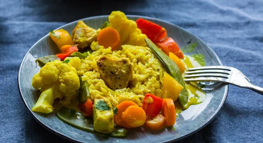 Ein Teller mit gelbem Reis, Blumenkohl, Karotten, Paprika und Erbsen. Ein köstliches Curry Geschnetzeltes, bereit zum Genießen.