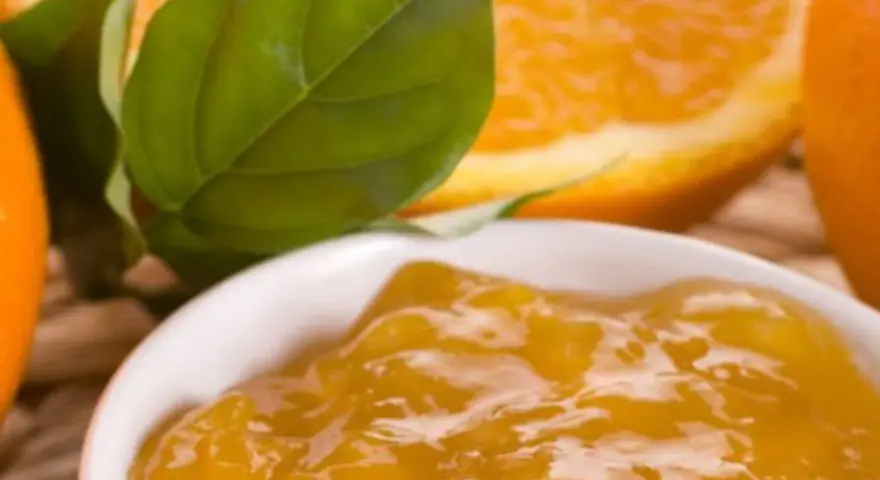 Una ciotola di marmellata di arance, con fette di arancia e foglie verdi sullo sfondo. Un'idea per un delizioso pesto al limone.