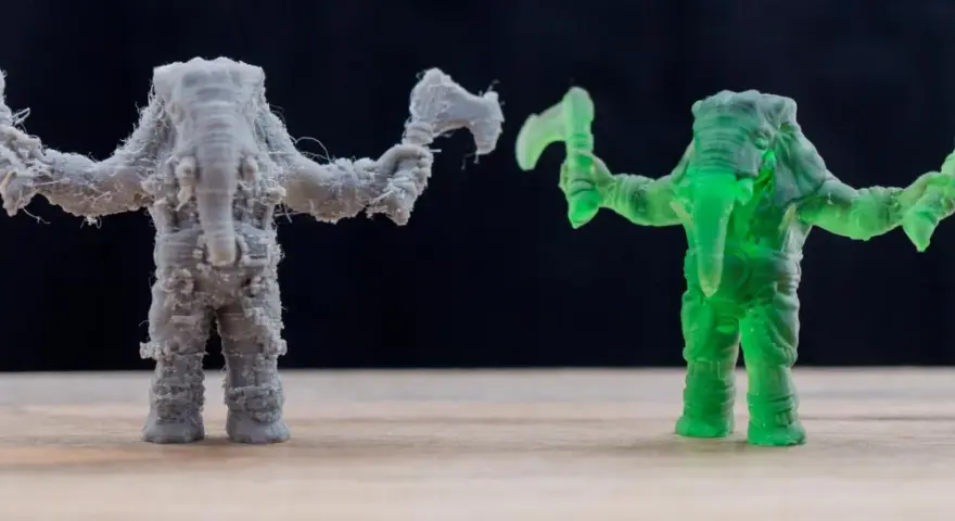 A grey FDM printed elephant warrior with stringing, and a translucent green resin printed elephant warrior, showcasing the difference between FDM vs resin printing.
