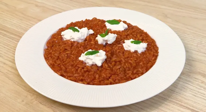 Un invitante risotto al pomodoro, arricchito da ciuffi di ricotta fresca e basilico, pronto per essere gustato.
