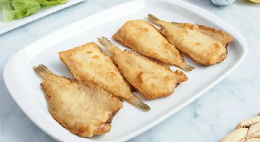 Cinco acedias fritas doradas y crujientes en una bandeja blanca, listas para disfrutar.