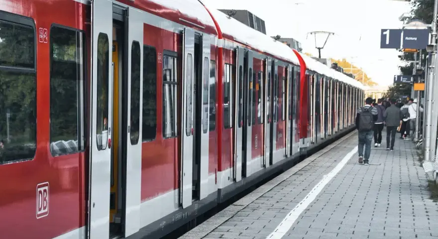 Czerwony pociąg na stacji. Ludzie czekają na peronie, zastanawiając się, jak zwrocic bilet.
