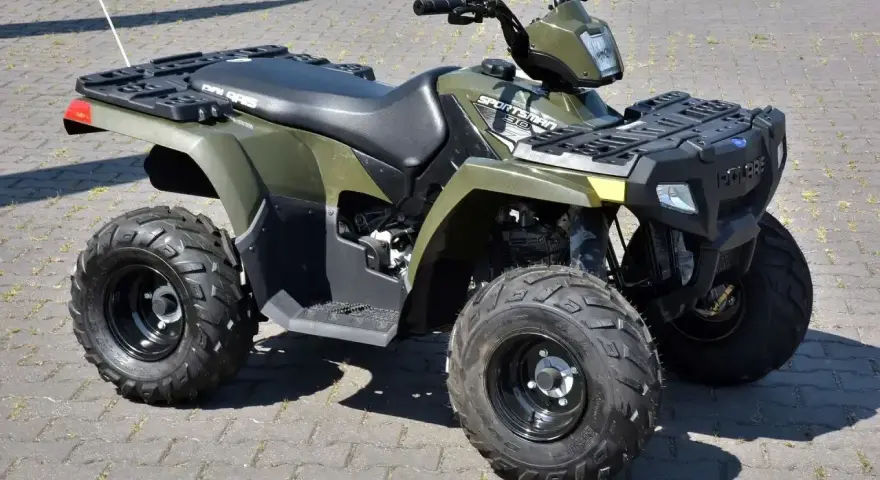 Zielony quad Polaris Sportsman 300 na kostce brukowej.
