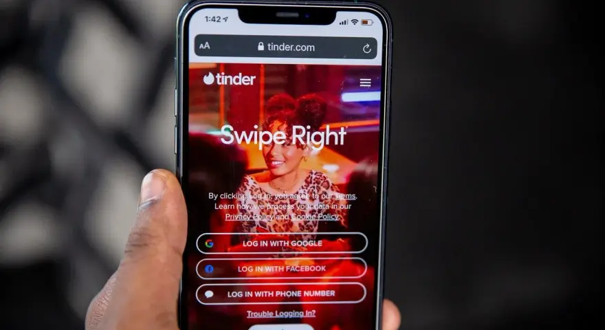 Telefon z aplikacją Tinder. Widoczne opcje logowania: Google, Facebook, numer telefonu. Czas na skróty na Tinderze!