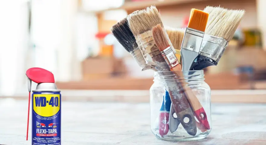 Un bote de WD-40 y un frasco de vidrio con varios pinceles sucios, listos para limpiar.