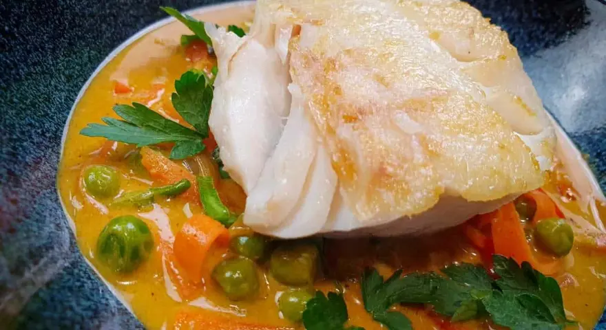 Aromatyczny curry z dorszem, podane z groszkiem i marchewką w kremowym sosie.