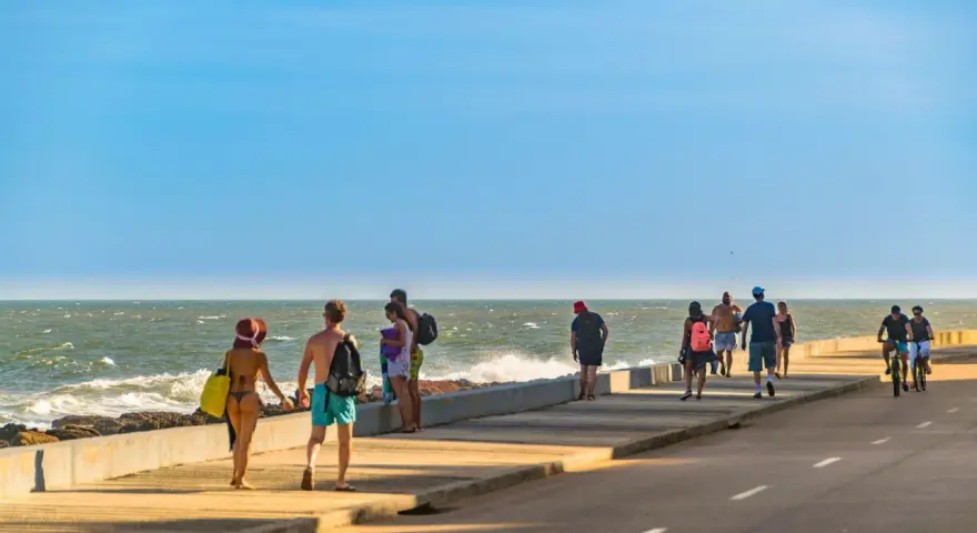 Ludzie spacerują i jeżdżą na rowerach wzdłuż promenady nad oceanem w słoneczny dzień.