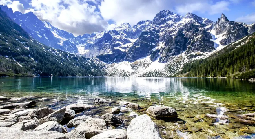 Morskie Oko, jedne z najpiękniejszych gór w Polsce, otoczone ośnieżonymi szczytami i zielonymi lasami, odbija się w krystalicznie czystej wodzie.