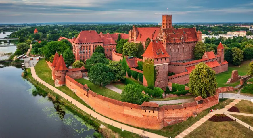 Malbork i okolice co zwiedzić? Potężny zamek krzyżacki nad rzeką, otoczony murami i zielenią, zaprasza do odkrywania historii.