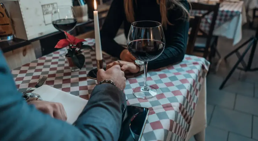 Romantyczna kolacja, świeca, wino i dłonie splecione na stole. Widać, jak angażuje się mężczyzna, skupiony na partnerce.