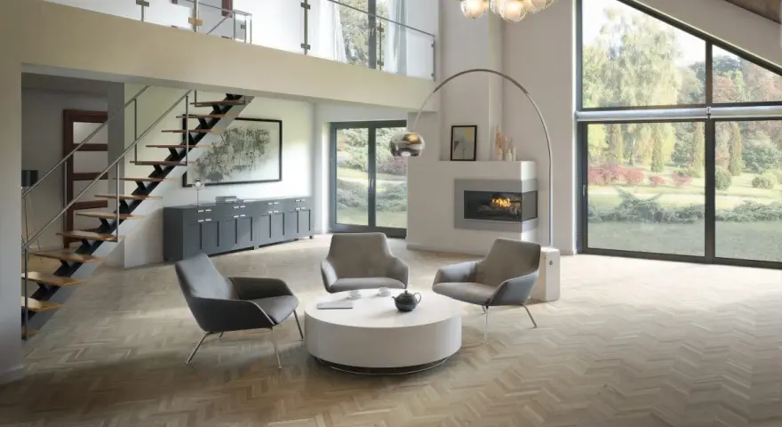 Salon moderne avec un **plafond cathédrale moderne**, escalier flottant, cheminée et grandes baies vitrées donnant sur un jardin.