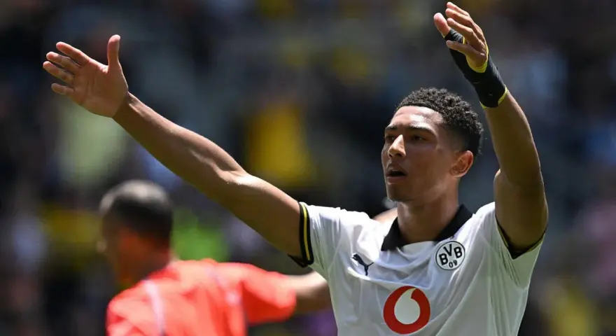 Jude Bellingham, con los brazos en alto, celebra un gol. El joven jugador del Dortmund, con su camiseta blanca, inspira a la afición.