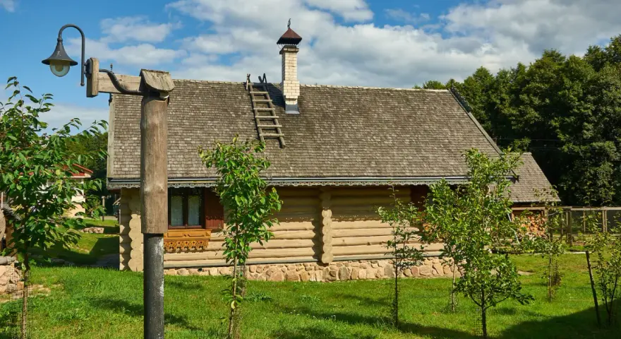 Drewniany dom z kamienną podmurówką i gontowym dachem, otoczony zielenią. To malownicze grunty rolne zabudowane, gdzie tradycja spotyka się z naturą.