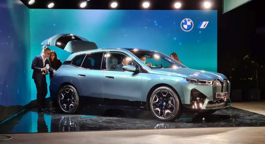 Jasnoniebieski elektryczny SUV BMW iX z otwartą klapą bagażnika na scenie.