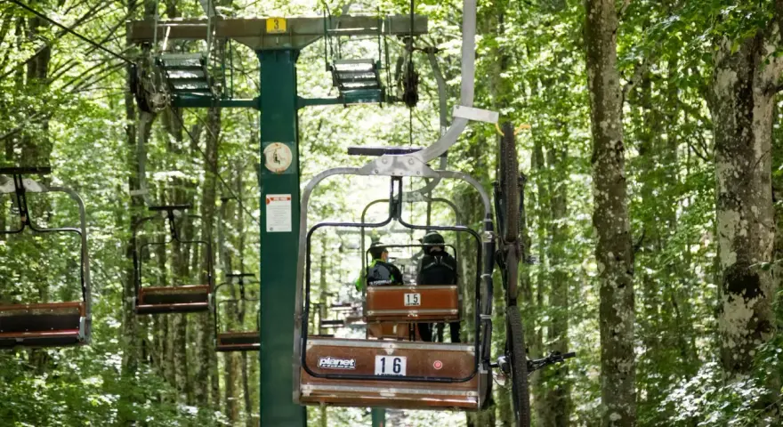 La funivia Monte Amiata trasporta due persone e una mountain bike attraverso un bosco lussureggiante.