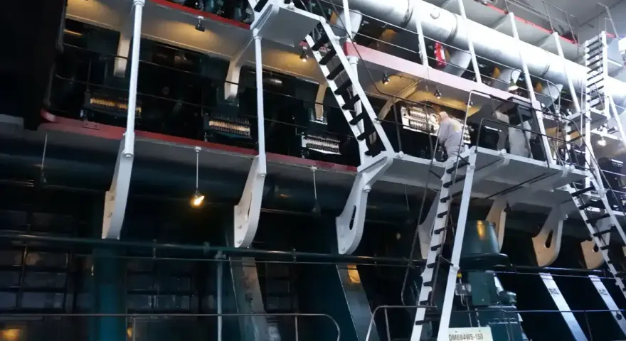 Ogromna, wielocylindrowa jednostka napędowa, prawdopodobnie największy silnik na świecie, z metalowymi schodami i platformami dla obsługi.