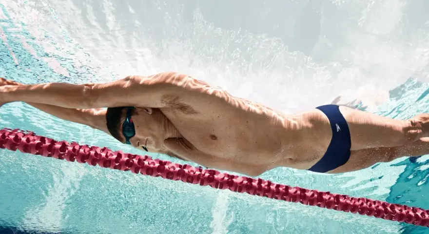 Un nageur en plein effort, profitant des bienfaits natation. La lumière joue sur son corps musclé, soulignant la puissance de ses mouvements sous l'eau.