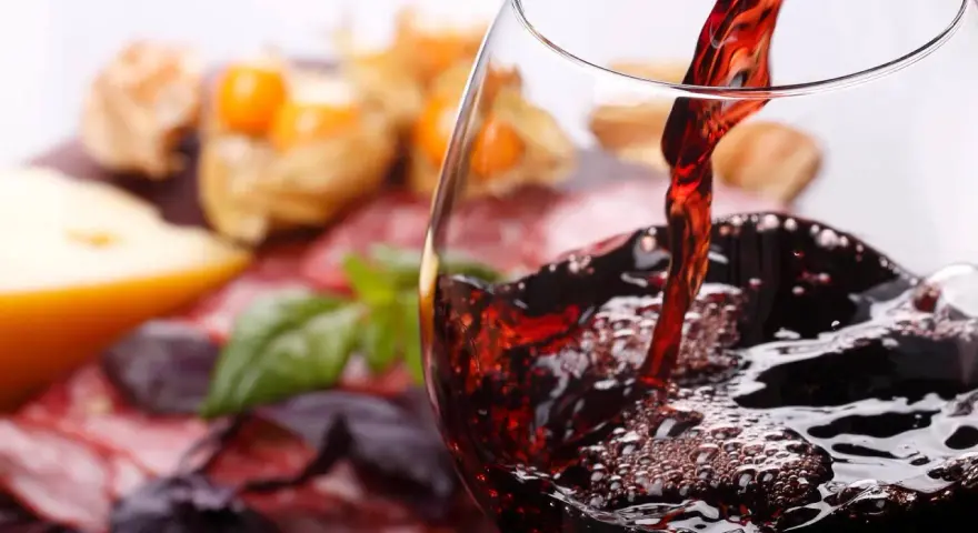 Rotwein wird in ein Glas gegossen, daneben Käse und Wurst. Welcher Wein hat am wenigsten Kalorien?