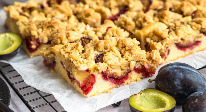 Saftiger Zwetschgenkuchen mit Streuseln, frisch gebacken und bereit zum Genießen. Daneben liegen frische Zwetschgen.