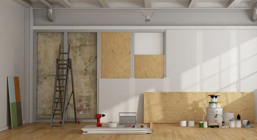 Chantier de rénovation avec panneaux de bois, échelle, outils et pots de peinture.
