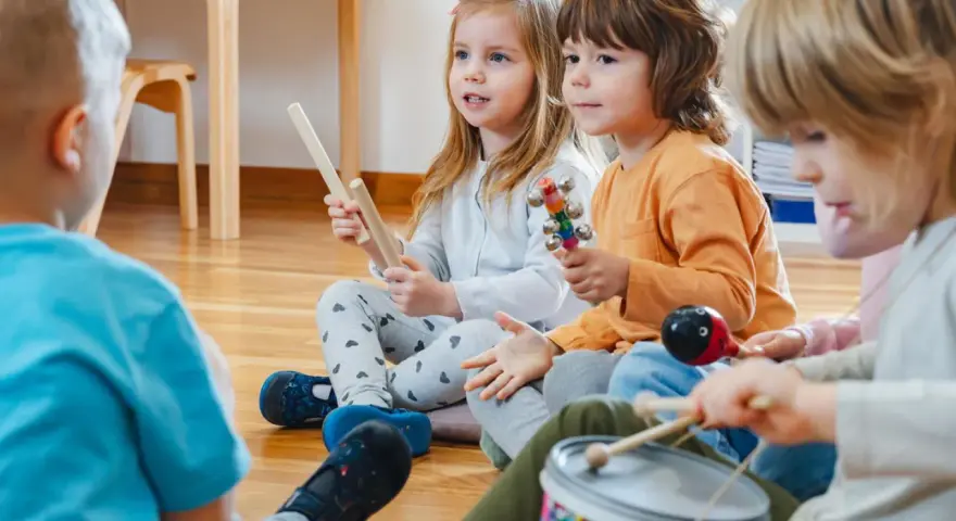 Kinder musizieren mit Holzstäben, Rasseln, einer Trommel und einem Maracas. Welche Instrumente gibt es?