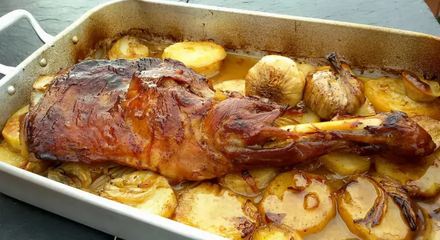 Delicioso cordero asado en una bandeja con patatas doradas y ajos enteros. Un festín para los sentidos.
