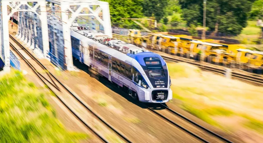 Nowoczesny pociąg PKP Intercity z niebieskim przodem mija biały most kolejowy.