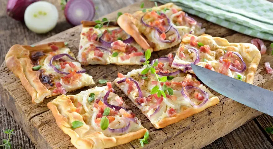 Kawałki pizzy z cebulą i boczkiem na drewnianej desce.