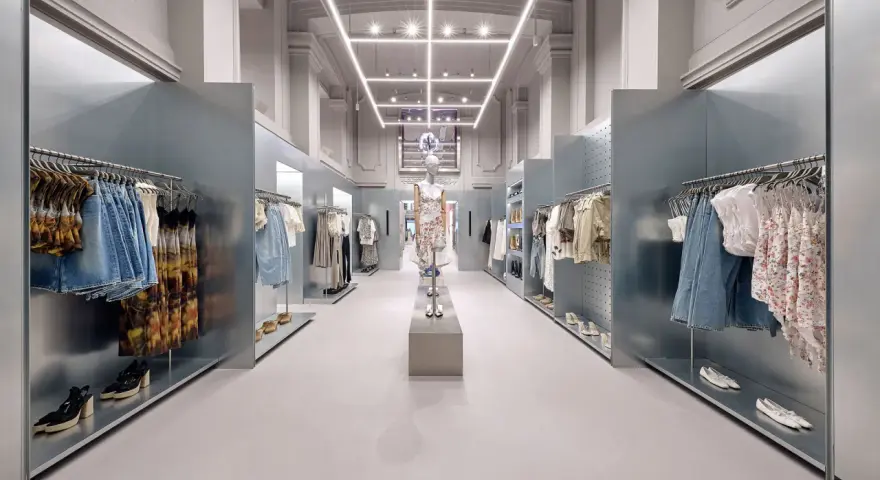 Nowoczesne wnętrze sklepu Bershka z wieszakami pełnymi ubrań i manekinem w centrum.