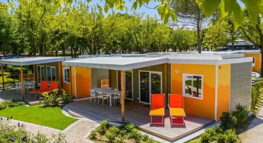 Kolorowe domki na kempingu, z tarasami i leżakami, otoczone zielenią. Prawdziwy camping garden paradiso!