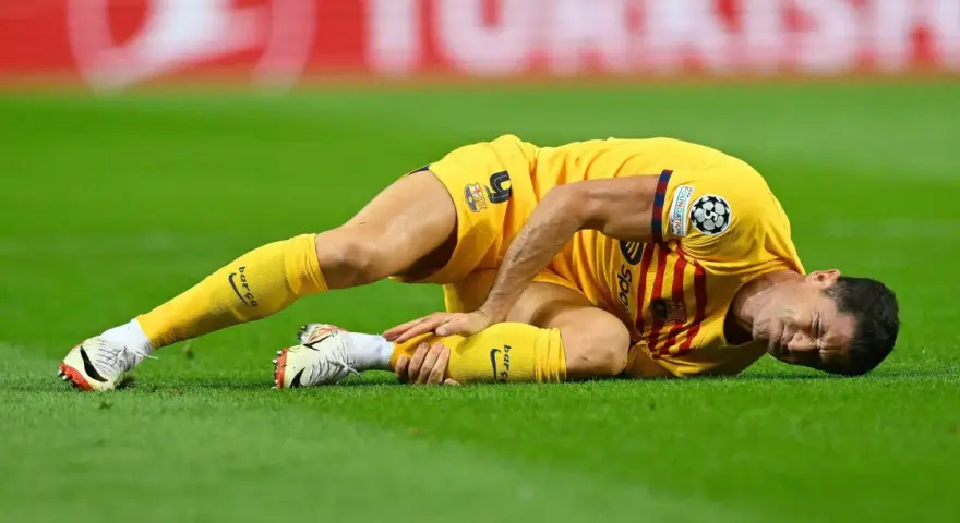Piłkarz w żółtej koszulce leży na trawie, trzymając się za nogę. Wygląda na to, że Robert Lewandowski kontuzja uniemożliwiła mu dalszą grę.