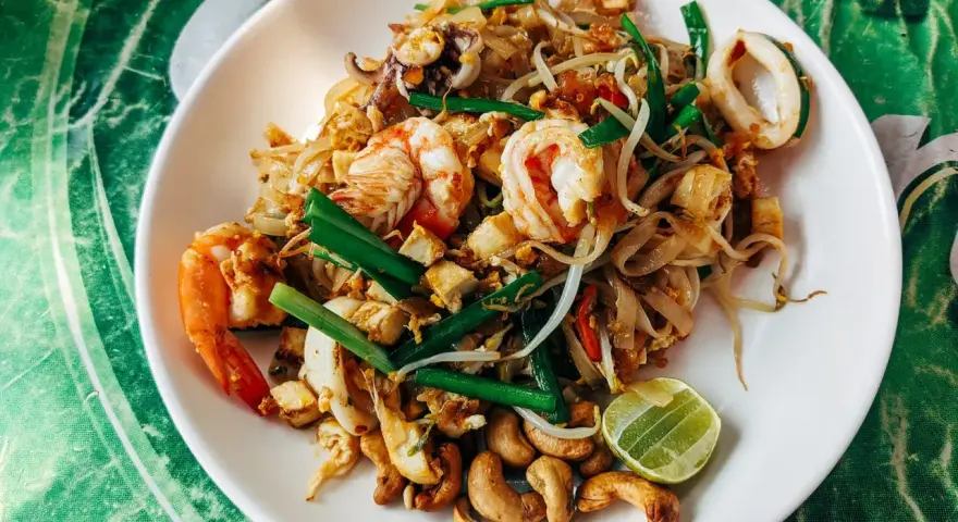 Pad thai z krewetkami, kalmarami, kiełkami i orzechami nerkowca. Widać też kawałek limonki, idealne pad thai składniki.
