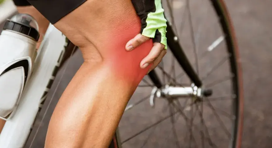 Cyclist holding knee with red pain indicator. Learn about cycling knee pain exercises to get back on the road.